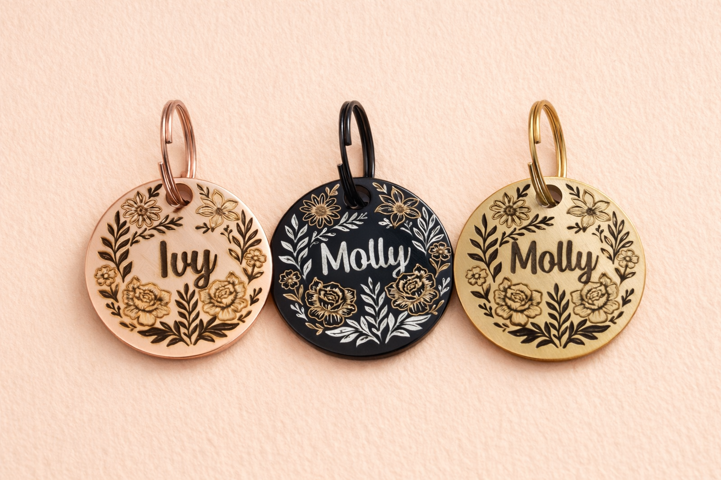 Three round metal tags with personalized names and floral designs, hanging on a light pink background.